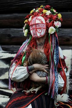 a woman in costume holding a chicken with flowers on her head and wearing a mask