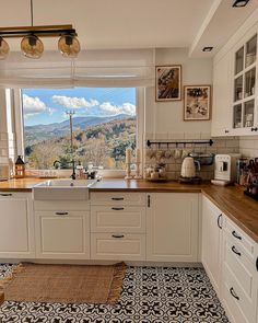 a kitchen with white cabinets and black and white tile flooring that has mountains in the background