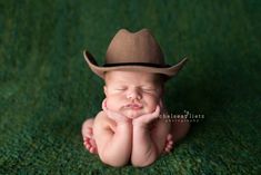 a baby is wearing a cowboy hat while laying on the ground with his hands under his chin