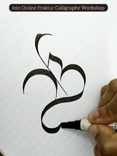 a person is writing on paper with a pen in their hand and there is a black ink drawing that looks like the letter s