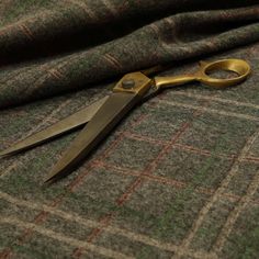 a pair of gold scissors laying on top of a green and brown plaid fabric,