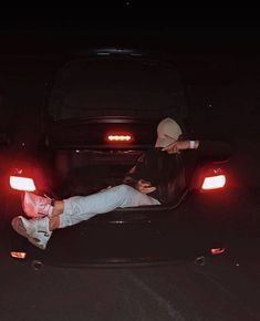 a person laying on the back of a car at night with their feet up in the trunk