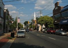 cars are parked on the street in front of shops and buildings with a steeple in the background