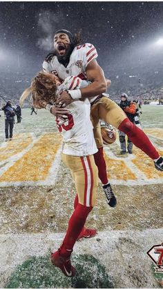 two football players hugging each other on the field in the snow with fans watching from the stands