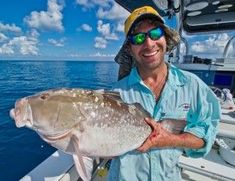 a man on a boat holding a large fish in his hands and smiling at the camera