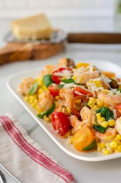 a white plate topped with shrimp, corn and tomato salad next to a slice of cheese