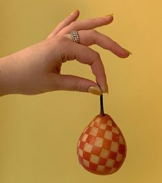 a woman's hand is holding an orange and white checkered fruit with a ring on it