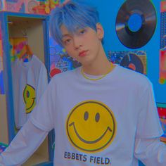 a young man with blue hair wearing a smiley face t - shirt in front of a record player