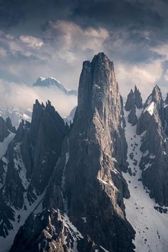 the mountains are covered in snow under a cloudy sky with some clouds above them,