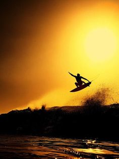 a person on a surfboard in the air above water at sunset or sunrise time