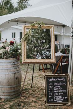 a sign that is sitting in the grass next to a barrel with flowers on it