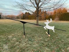 a white deer on a black rail in the middle of a field with trees and grass