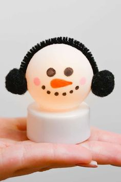 a hand holding a small snowman with black hair on it's head and nose