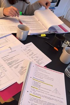 a woman sitting at a table with papers and coffee mugs on top of it