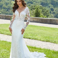 a woman in a white wedding dress standing on the grass with her arms behind her back