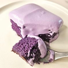 a piece of cake with purple icing on a white plate and a fork next to it