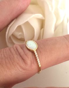 a close up of a person's hand holding a ring with a white rose in the background