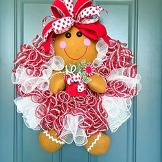 a red and white wreath with a teddy bear hanging from it's front door