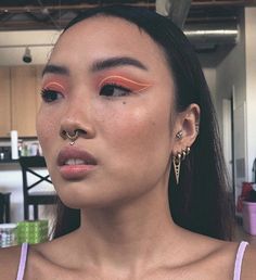 a woman with orange and pink makeup looks at the camera while wearing gold ear piercings