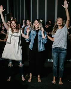 three women standing in front of a crowd with their hands up