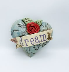 a heart shaped box with a red rose on it and the word dream written in blue