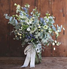 a bouquet of blue and white flowers in a glass vase on a wooden table next to a wood wall