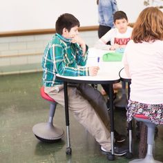 three children are sitting at a table with their teacher