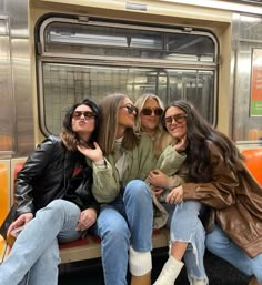 three women are sitting on a subway car and posing for the camera with their hands in their pockets