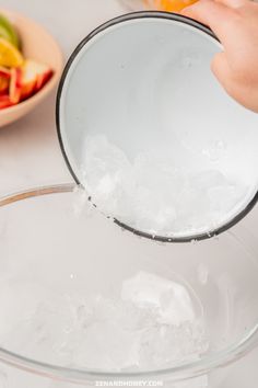 someone is pouring ice into a bowl with fruit in it and another bowl behind them