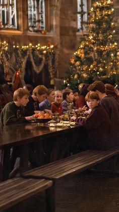 a group of people sitting at a table eating food in front of a christmas tree