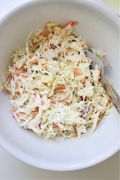 a white bowl filled with coleslaw and carrots next to a silver spoon