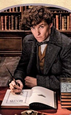 a young man sitting at a desk with an open book and pen in his hand