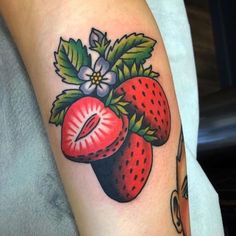 a close up of a person's arm with a strawberry and leaves tattoo on it