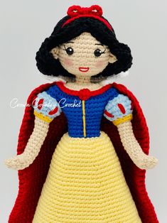 a crocheted snow queen doll with red cape and yellow dress is posed on a white surface