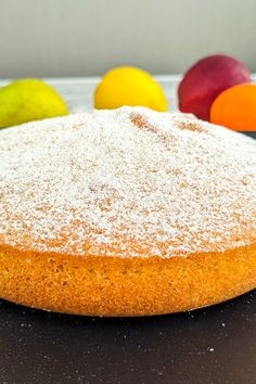 a cake with powdered sugar on top and fruit in the background