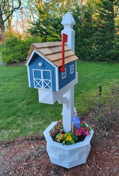 a mailbox shaped like a house with a flag on top and flowers in the bottom