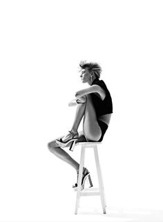 a black and white photo of a woman sitting on a stool with her legs crossed