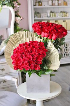 two vases with roses in them on a table next to a chair and mirror