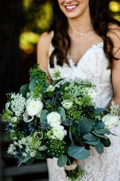 a woman holding a bouquet of flowers and greenery in her hands smiling at the camera