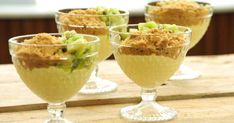 three glasses filled with dessert sitting on top of a wooden table