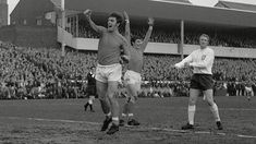 two men are playing soccer in front of an audience at a stadium with their hands up