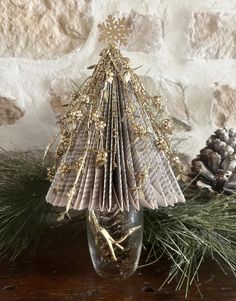 a small christmas tree made out of folded book pages in a vase with pine cones