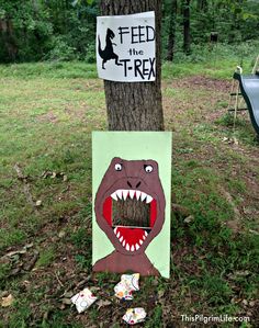 a sign that says feed the t - rex next to a tree with an image of a dinosaur on it