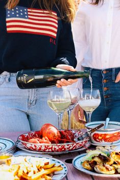 a woman pouring wine into a glass at a table full of food