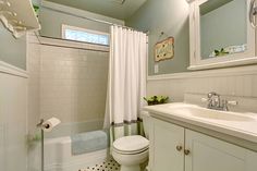 a white toilet sitting next to a bath tub under a bathroom mirror with a skylight