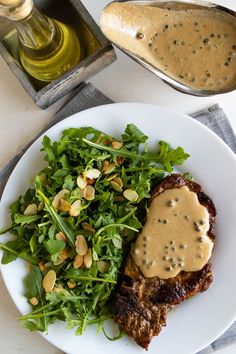 a white plate topped with meat covered in gravy next to a green salad