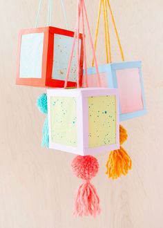 three colorful boxes hanging from strings with pom - poms attached to them on a wall