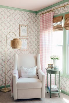 a white chair sitting in front of a window next to a table with a lamp on it