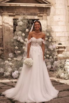 a woman in a wedding dress standing on a stone walkway with flowers and greenery behind her