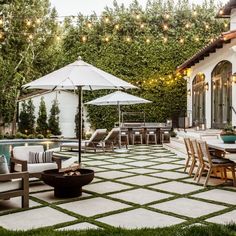 an outdoor patio with tables, chairs and umbrellas next to a swimming pool surrounded by greenery